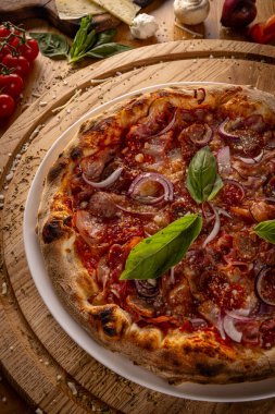 Lezzetli ev yapımı pepperoni pizza fesleğen garnitürlü, ahşap bir masada servis ediliyor, arka planda malzemeler var.