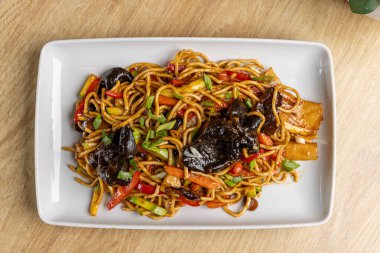Ahşap bir masada servis edilen siyah mantarlı lezzetli kızarmış sebze chow mein.
