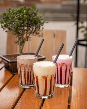 Çikolata soslu üç milkshake bir restoranın ahşap masasında duruyor.