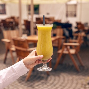 Garson, sıcak bir yaz gününde açık bir kafede serinletici bir tropikal meyve suyu tutuyor.