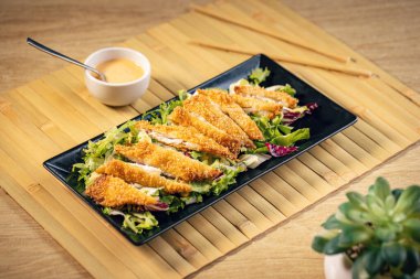 Kızarmış tavuk şeritleri marul yatağında yanında sos ile servis edilir.