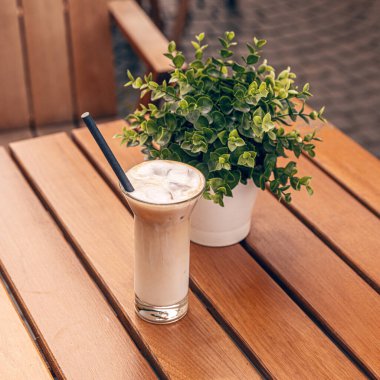 Açık bir kafe terasındaki ahşap bir masada otururken buzlu kahve tazeleniyor.