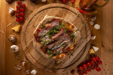 Güneşte kurutulmuş domatesli zanaatkar pizza, prosciutto, roka ve peynir, kırsal ahşap üzerinde servis edilir.