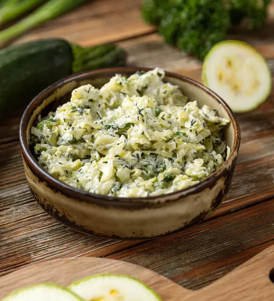 Bir kase rendelenmiş kabak salatası, dereotlu ve maydanozlu köy ahşabı masa.