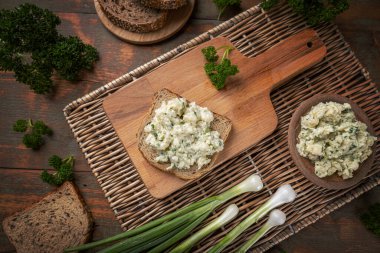 Karnabahar salatası bir dilim kızarmış ekmeğin üzerine serpilmiş yeşil soğan ve tahta kesme tahtasının üzerinde maydanoz.