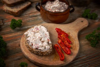 Paprika krem peyniri, kızarmış ekmeğin üzerine sürülmüş kırmızı biber dilimleri ile ahşap tahta üzerinde.