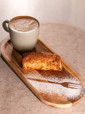 Tahta tepside duran lezzetli, çıtır çıtır hamur işi ve kapuçino, krema çatal dizaynı ile süslenmiş.