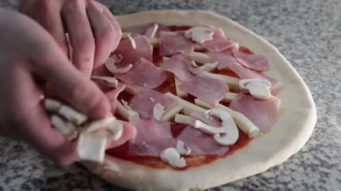 Pizza şefi pizza hamuruna mantar ve jambon ekliyor.