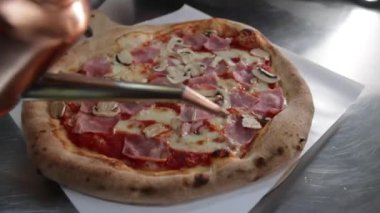 Jambon, mantar ve mozzarella peyniri ile kaplı bir pizzanın üzerine zeytin yağı dökülüyor.