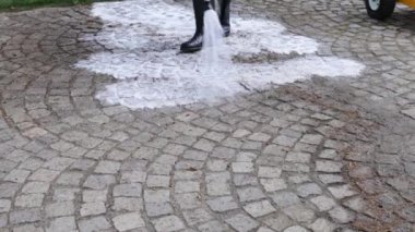 İşçi, yüksek basınçlı su jetiyle taş kaldırımları temizliyor.