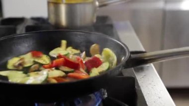 Profesyonel şef, taze sebzeleri gaz sobasında sıcak bir tavaya ustalıkla atıyor.