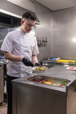 Genç aşçı çeşitli malzemelerle restoranda taze salata hazırlıyor.