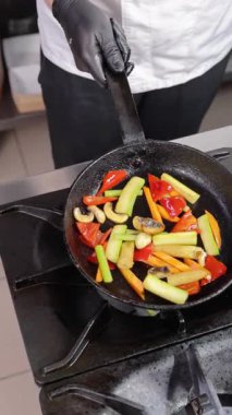 Şef sıcak tavaya renkli sebzeler atıyor.