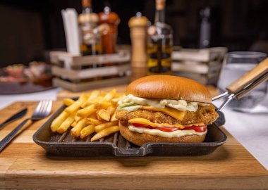 Lezzetli hamburger, tavuklu eritilmiş peynir, domates, marul ve patates kızartması bir restoranda servis ediliyor.