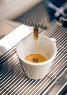 Profesyonel kahve makinesi beyaz fincana espresso dolduruyor.