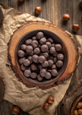 Çikolata kaplı fındıklar, ahşap bir yüzeye yerleştirilmiş bir kasede sunuluyor, tatlı ve kırsal bir mutfak sahnesi yaratıyor.