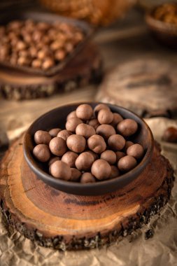 Çikolata kaplı fındıklar, ahşap bir yüzeye yerleştirilmiş bir kasede sunuluyor, tatlı ve kırsal bir mutfak sahnesi yaratıyor.