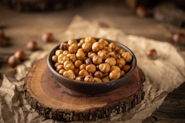 Kavrulmuş fındıklar ahşap bir tahtanın üzerine koyulmuş koyu bir kâseyi doldurur ve samimi bir sonbahar sahnesi yaratır.