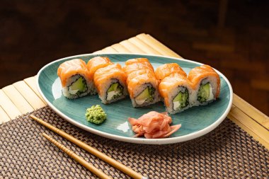 Lezzetli Philadelphia uramaki suşi ruloları turkuaz bir tabakta wasabi, zencefil turşusu ve çubuklarla servis edilir.