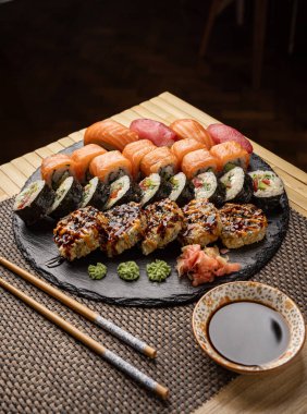 Suşi seti soya soslu, zencefil ve wasabi turşulu siyah tahtada servis edilir.