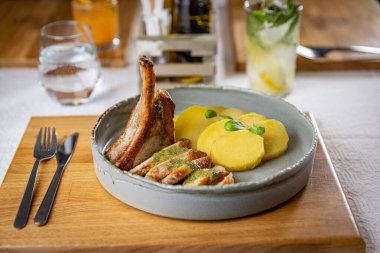 Dilimlenmiş patates ve pesto sosuyla servis edilen leziz ızgara domuz pirzolası ve yanında da ferahlatıcı bir içecek.