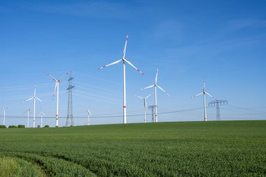 Yeşil tarım arazisindeki elektrik hatları ve rüzgar türbinleri