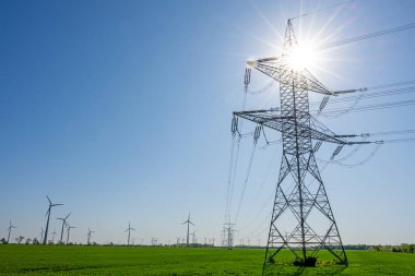 Arkasında güneş olan bir elektrik direği ve Almanya 'da görülen rüzgar türbinleri.