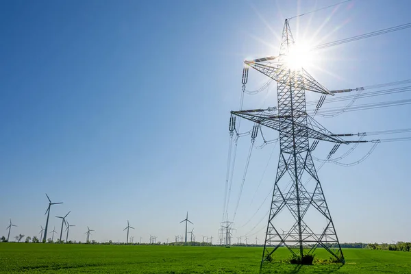 Ein Strommast Mit Der Sonne Hintergrund Und Windrädern Hintergrund Deutschland lizenzfreie Stockbilder