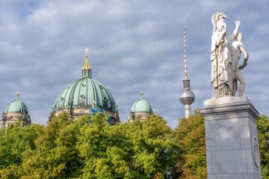Ağaç tepe örtüleri, katedralin kubbesi, beyaz bir heykel ve Berlin, Almanya 'da görülen ünlü TV kulesi.