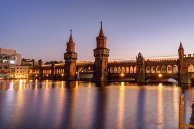 Oberbaumbruecke Nehri 'nin üzerinde Alacakaranlıkta Berlin' de bir metro ile yayıldı