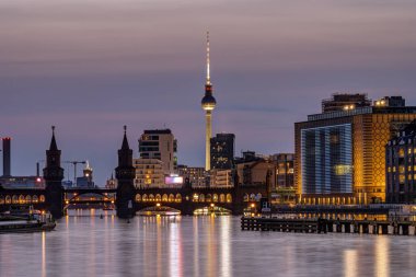 Berlin ve nehir, Oberbaum Köprüsü ve ünlü Televizyon Kulesi ile alacakaranlıkta batıyor.