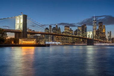 Ünlü Brooklyn Köprüsü ve New York 'ta alacakaranlıkta aşağı Manhattan' ın ufuk çizgisi.