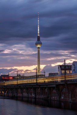 Meşhur Televizyon Kulesi ve nehir. Alacakaranlıkta Berlin 'deki banliyö trenini bulanıklaştıran bir hareketle Spree Nehri.
