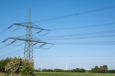 Almanya 'da arkada elektrik hatları ve rüzgar türbinleri olan elektrik direği görülüyor.