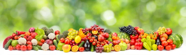 Bright multi-colored berries, fruits and vegetables on green blurred background.