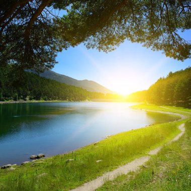 Beautiful sunrise over blue lake and mountains covered with coniferous forest.