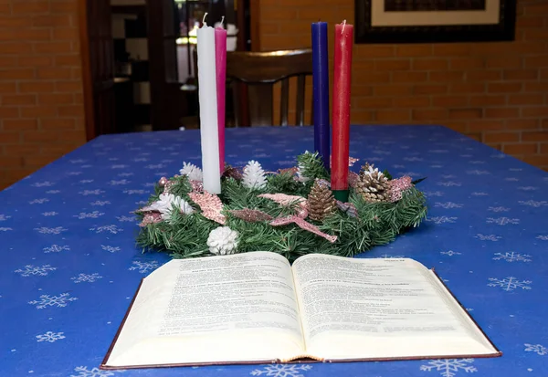 View of a christmas advent crown with a bible in front of it on a dining table