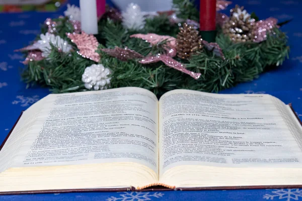 Close up view of a christmas advent crown with a bible in front of it on a dining table