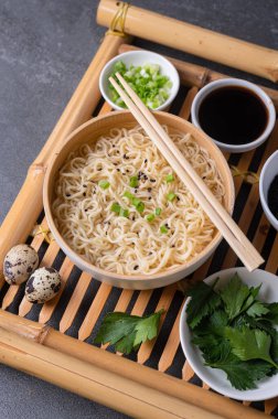 Beyaz bambu tabağı (kase) yumurta eriştesi ve malzemelerle birlikte koyu mermer bir zemin üzerinde bambu servis tepsisi üzerinde servis edilir. Asya geleneksel fast food