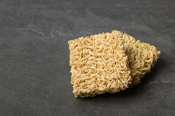Square dry egg noodles in a briquette on a gray stone marble (slate) background. Asian fast food.