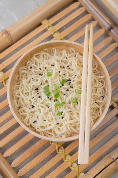 White bamboo plate (bowl) with egg noodles and plates with ingredients for it on a bamboo serving tray against a light background. Asian traditional fast food