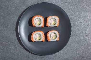Suşi, somon, avokado ve salatalıkla birlikte siyah bir taşın üzerinde yuvarlak bir tabakta yuvarlanır. Asya geleneksel yemekleri.