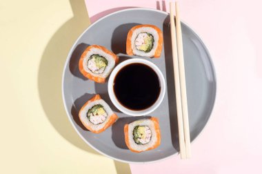 Somonlu Japon suşisi, parlak sarı-pembe arka planda ejderha ruloları. Pop sanat. Gri tabakta lezzetli atıştırmalıklar ve yemek çubukları. Geleneksel Asya yemekleri