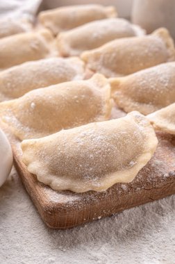 Raw dumpling with potatoes. Preparation dumplings on a light background on a wooden board. Fresh, handmade Ukrainian dumplings. National traditions, masna. Homemade dough products, craft cooking.
