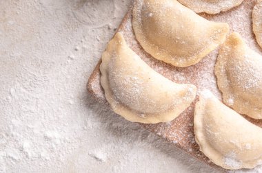 Raw dumpling with potatoes. Preparation dumplings on a light background on a wooden board. Fresh, handmade Ukrainian dumplings. National traditions, masna. Homemade dough products, craft cooking.