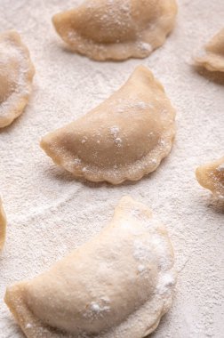 Fresh dumplings in flour on a light background. Pattern, background. Homemade craft production, national traditions, Ukrainian cuisine