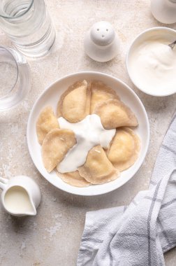 Fresh boiled dumplings in a light plate on a light background. Pattern, background. Homemade craft production, national traditions, Ukrainian cuisine