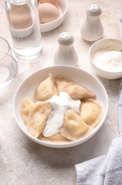 Fresh boiled dumplings in a light plate on a light background. Pattern, background. Homemade craft production, national traditions, Ukrainian cuisine