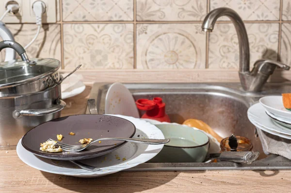 Messy kitchen with dirty dishes piled up in the sink and on the counter. Modern kitchen with white facades in the Scandinavian style