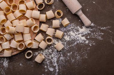 Kahverengi arka planda el yapımı makarna bu fotoğrafın konusu. Erişteler çeşitli şekil ve boyutlarda ve taze ve pişmemiş görünüyor. Buğdaydan ev yapımı makarna.